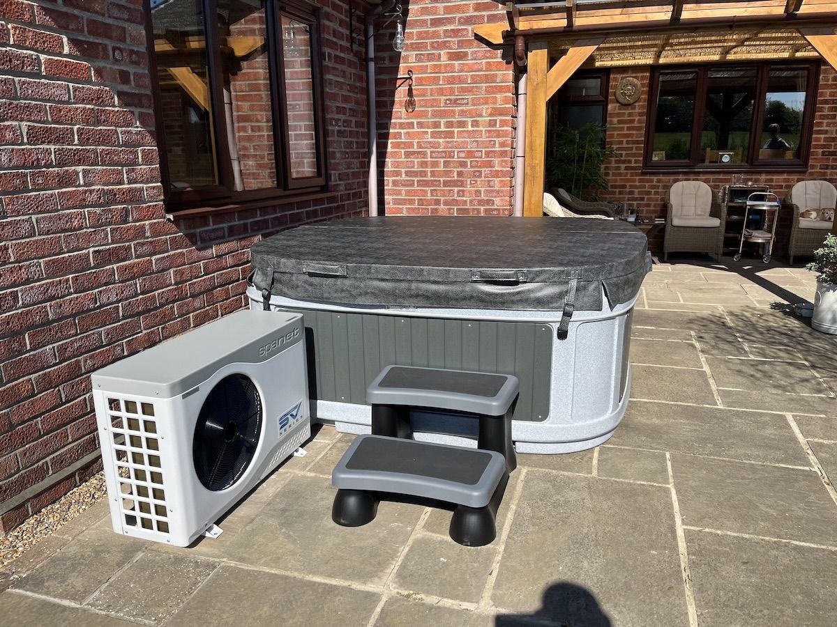 Heat pump beside hot tub on paved patio — tidy side install with easy service access